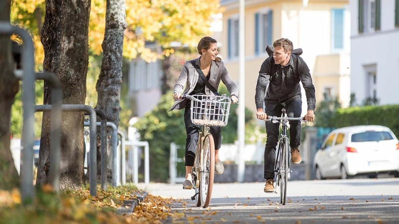 Zwei Radfahrer:innen fahren im Herbst zusammen Fahrrad
